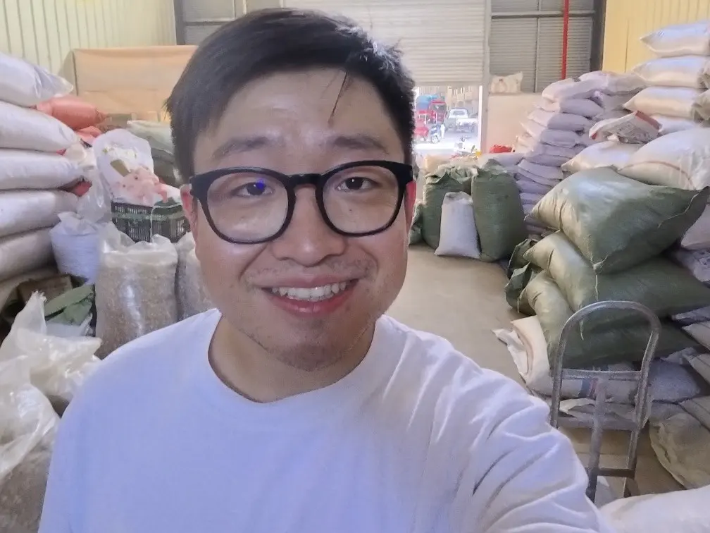 Fu Yang sonriendo en un almacén, con sacos de especias apilados detrás de él