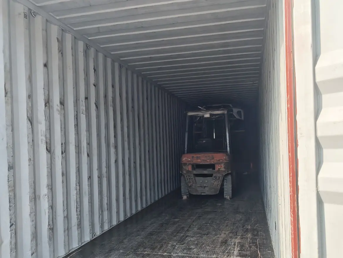Empty shipping container seen from its open doors, with a forklift parked inside at the far end