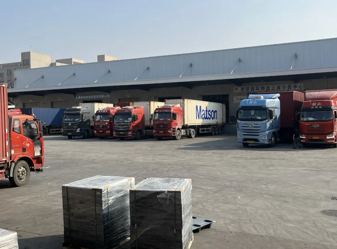 Container trucks lined up at dock bays, with shrink-wrapped pallets waiting in the yard