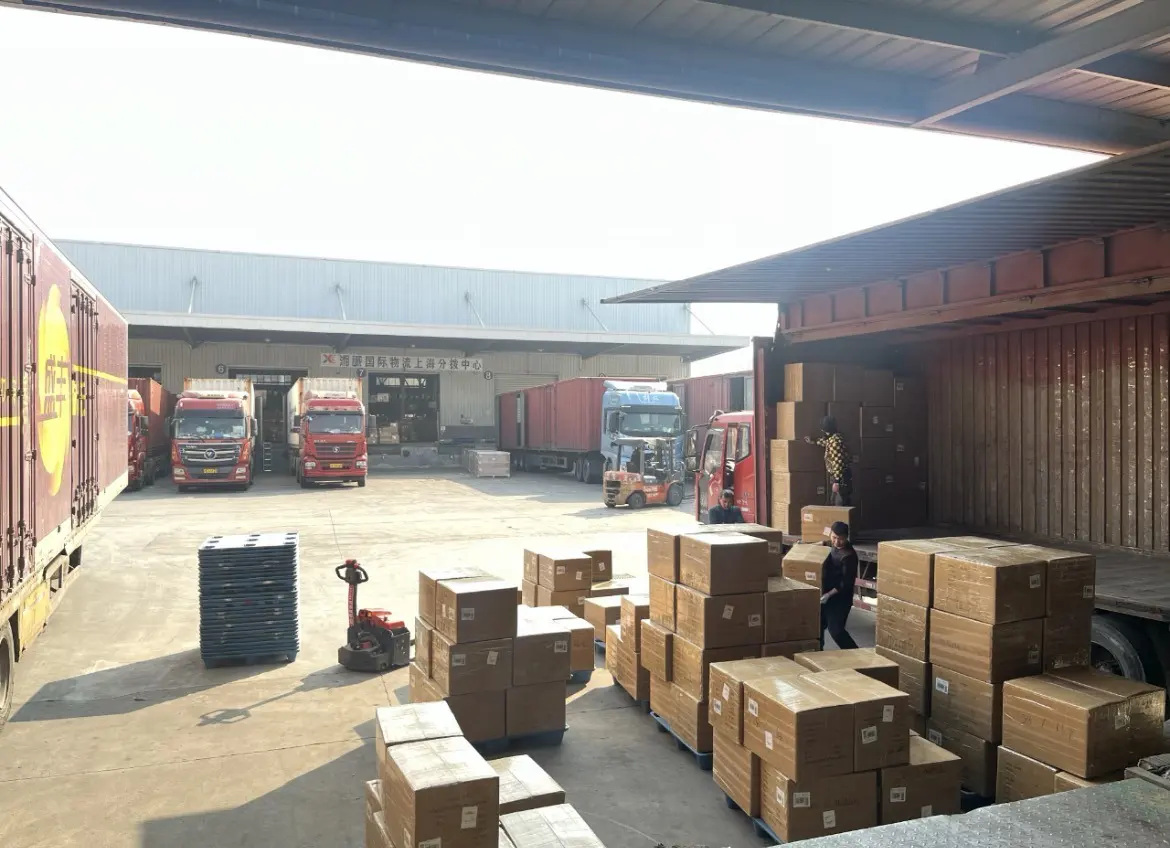 Cartons stacked on pallets in a loading yard while a container is loaded at the dock